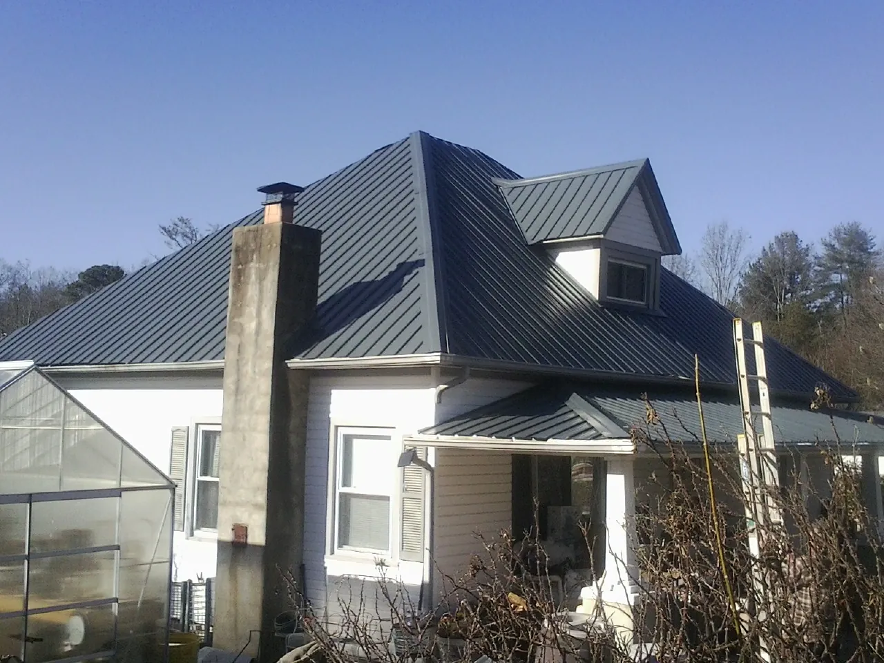 Dark blue standing seam metal roof on a white farmhouse with dormer — Slate & Tile Roof Repair by Roofing Brothers in Paint Bank