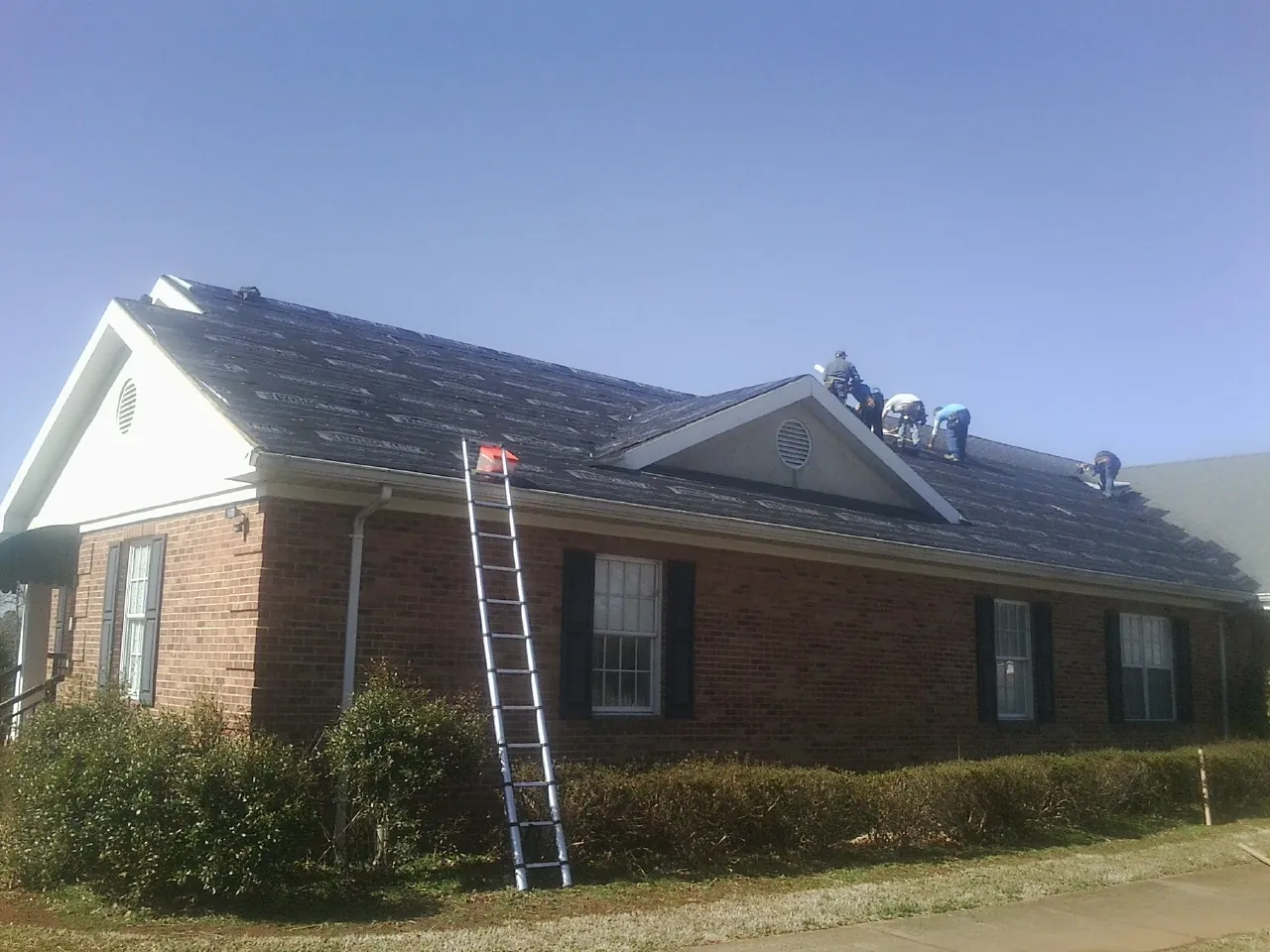 Crew tearing shingles off a brick ranch roof with a ladder set — Emergency Roof Repair work by our crew in Paint Bank