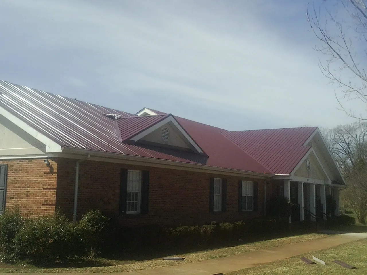 Red metal roof with gabled entries on a long brick building, from a Hail Damage Roof Repair job in Paint Bank