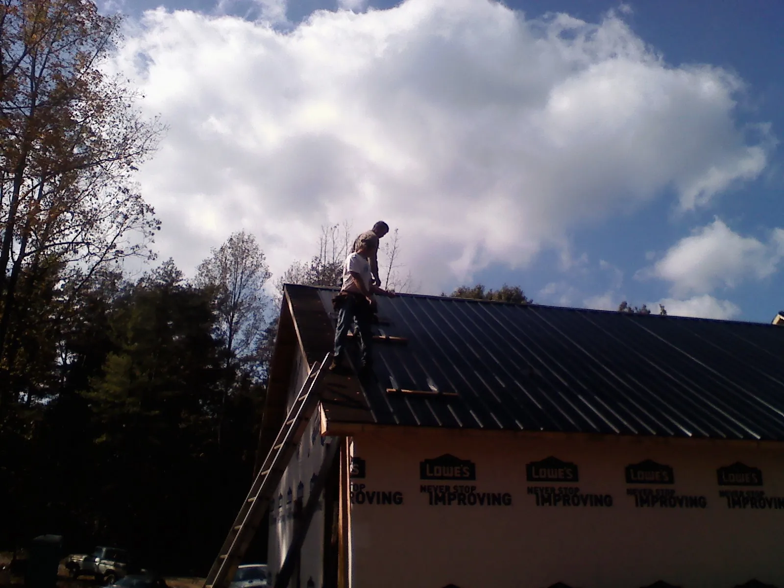 Roofer fastening dark metal panels high against a cloudy sky, from a Roof Inspection job in Paint Bank