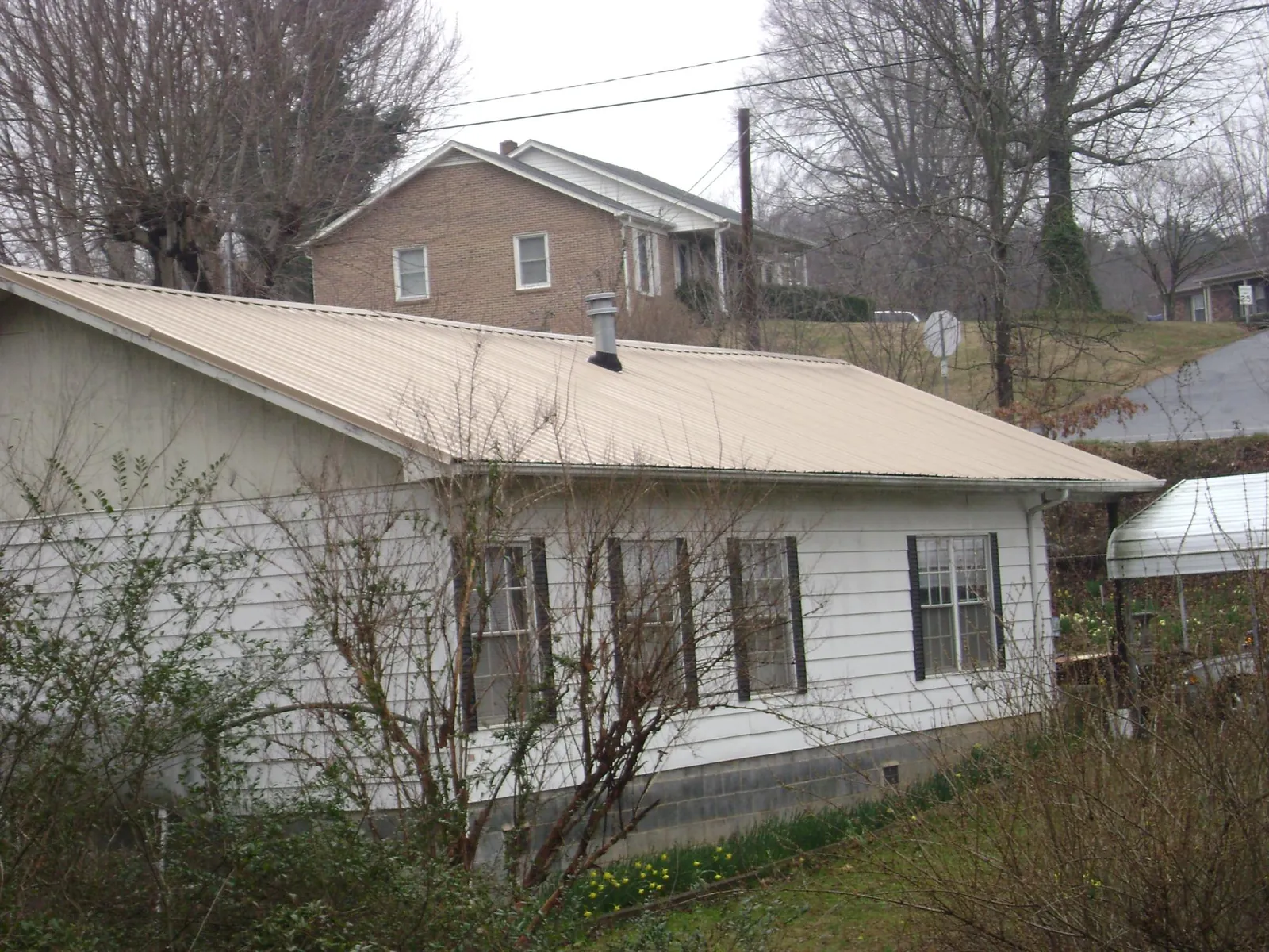 Tan metal roof on a white sided house set into a hillside — Commercial Roofing by Roofing Brothers in Paint Bank